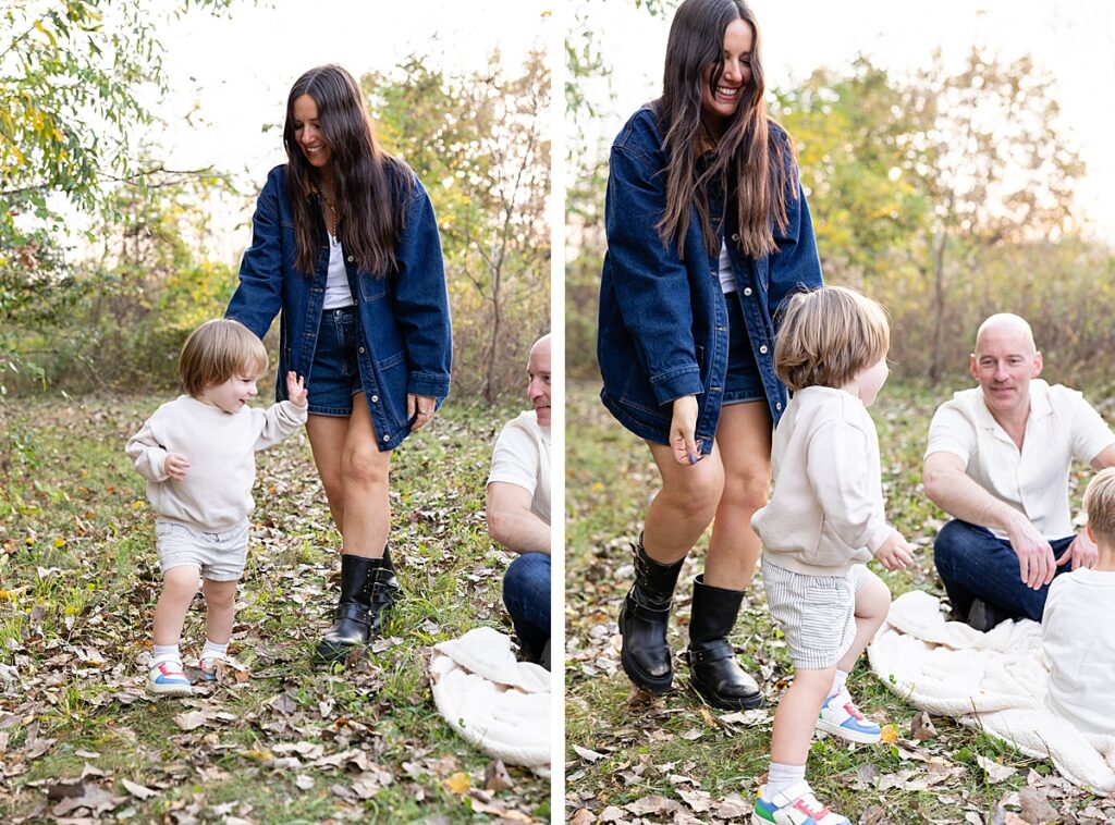 Mother in denim jacket walking hand-in-hand with her toddler through a wooded clearing during a fall session.