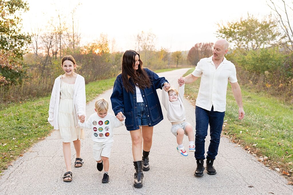Parents and three kids walking hand-in-hand along a path, swinging the youngest child between them.