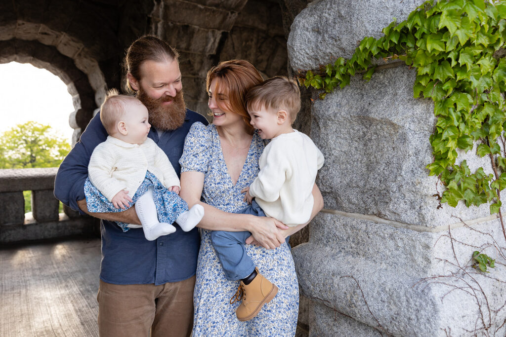 Parents laughing with their children beside an ivy-covered stone wall at Lincoln Park Nature Boardwalk.