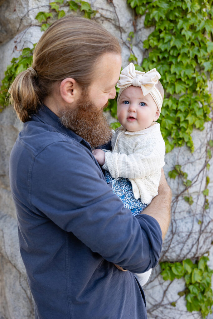 Father holding his baby daughter near an ivy-covered stone wall at Lincoln Park Nature Boardwalk.