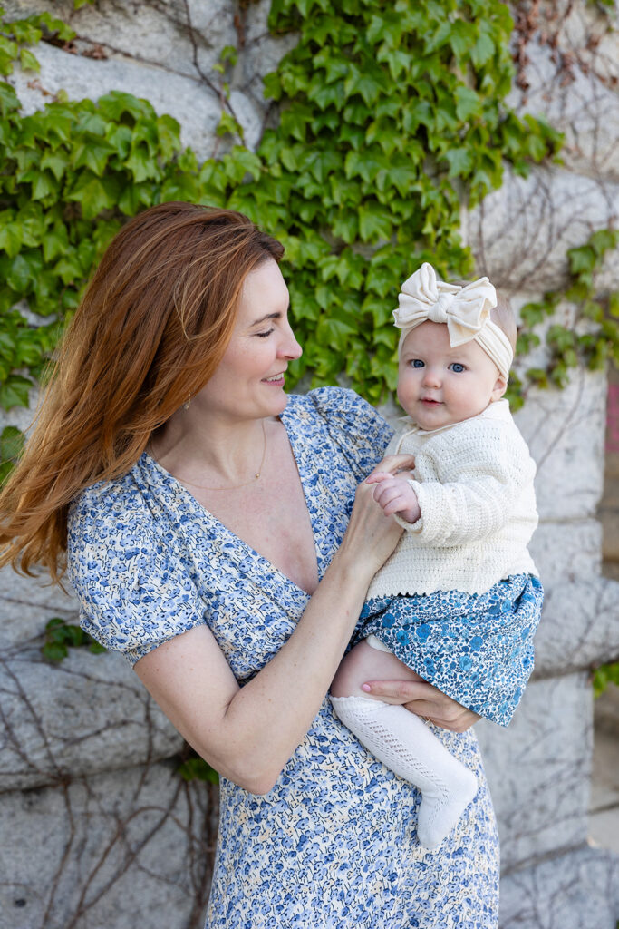 Mother holding her baby daughter beside an ivy-covered stone wall at Lincoln Park Nature Boardwalk.