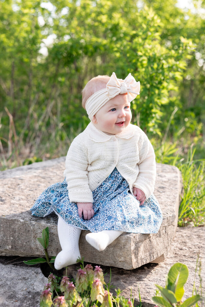 Baby girl sitting on a large stone surrounded by spring greenery at Lincoln Park Nature Boardwalk.