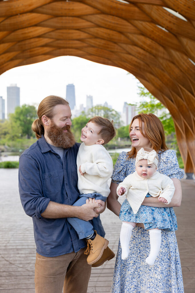 Family portrait with a Chicago family photographer beneath the stone pavilion at Lincoln Park Nature Boardwalk and the Chicago skyline.